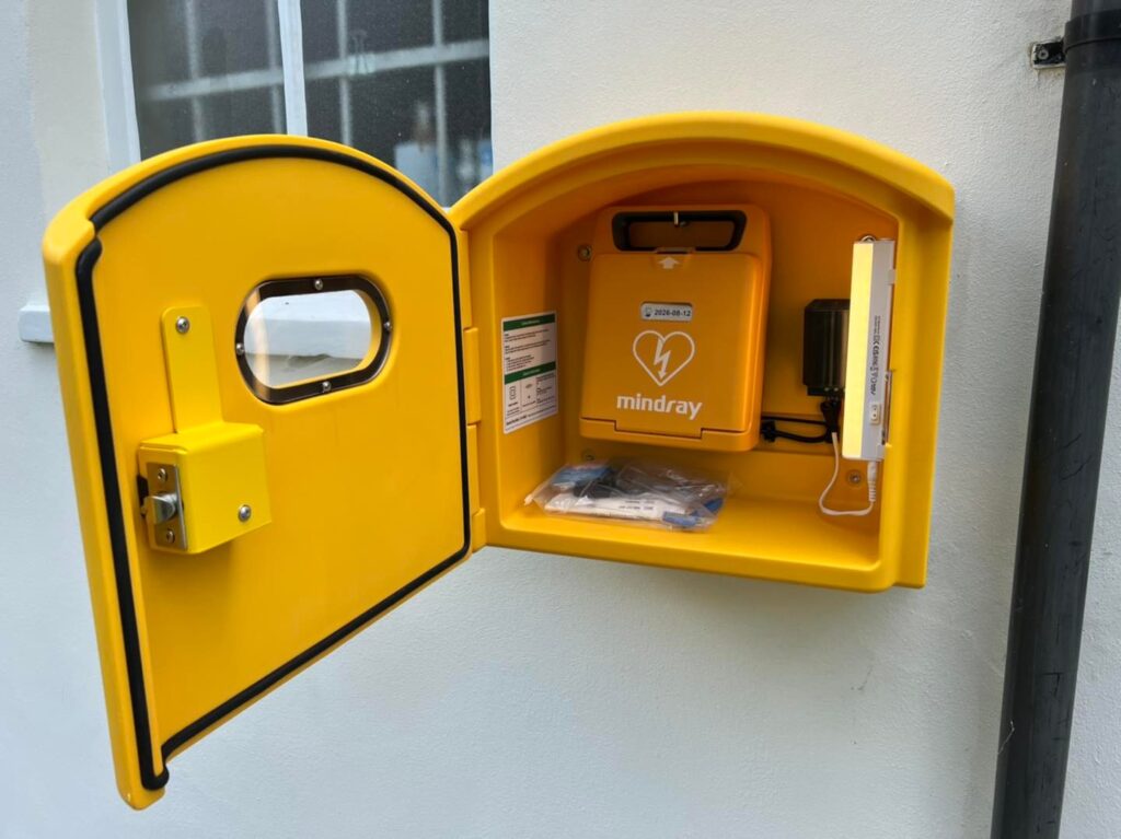 Mindray AED defibrillator mounted in a bright yellow box, showcasing the device’s availability for emergency use, featured in the post 'Mindray Defibrillator vs. Competitors'