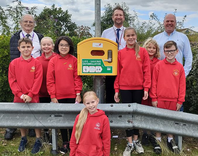 Students and staff stand proudly next to a newly installed life-saving defibrillator outside their UK school, provided by Defib World