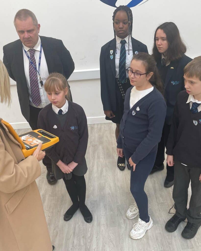 Students and staff learning how to use a defibrillator (AED) during a safety training session at a UK school, supported by Defib World