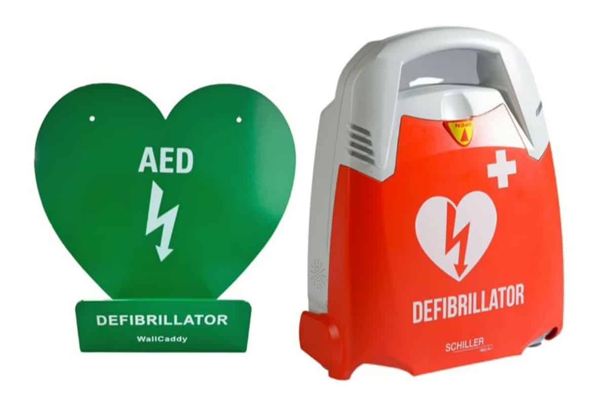 A SCHILLER FRED PA-1 defibrillator in a closed red and white case next to a green heart-shaped AED defibrillator wall caddy.