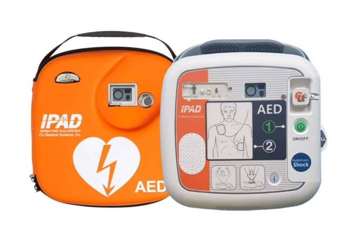 An orange iPAD SP1 defibrillator carry case next to the defibrillator, showing a simple green on/off button and diagram for pad placement.