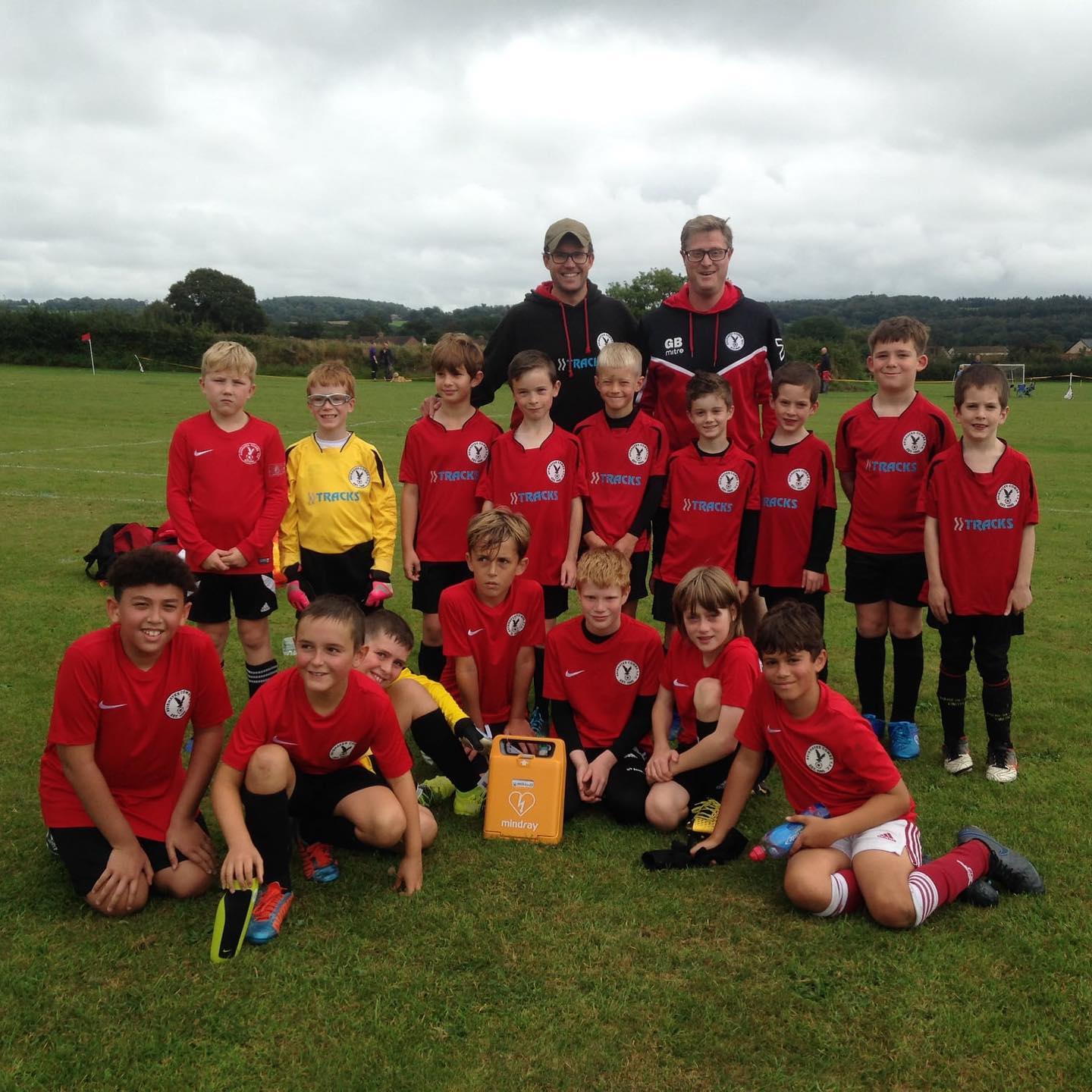 A youth soccer team posing for a group photo on the field with a defibrillator in the foreground. This image emphasizes the importance of having life-saving defibrillators readily available in sports settings, ensuring quick response in case of cardiac emergencies.