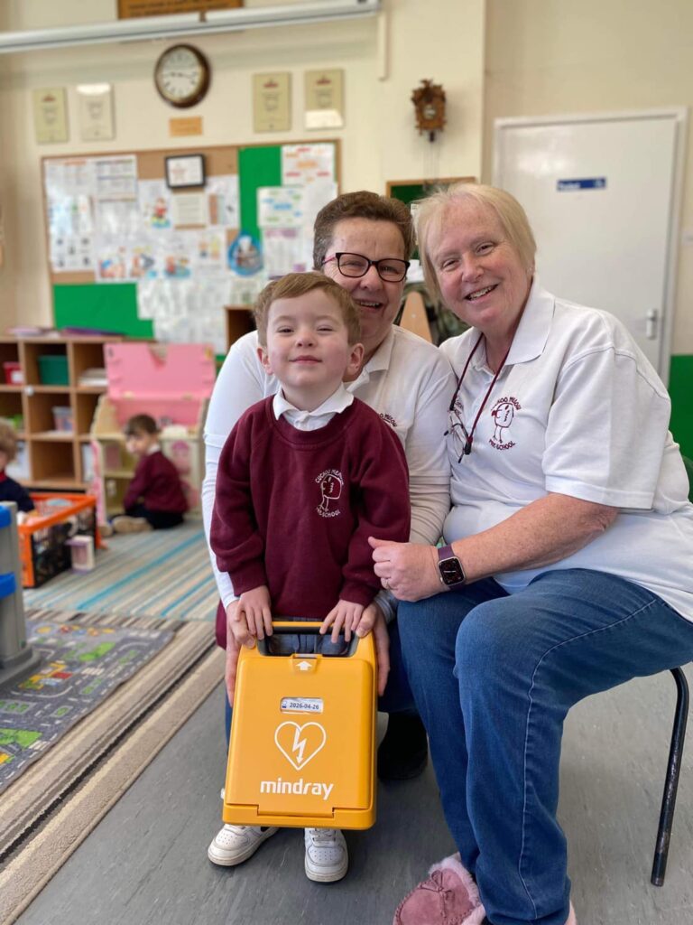 Child with two adults holding a Mindray AED defibrillator, emphasizing the importance of AEDs in schools and childcare settings