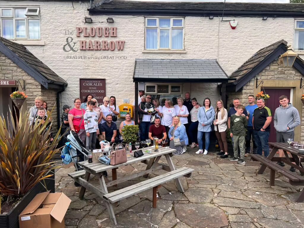 Group of people gathered outside The Plough & Harrow pub, receiving AED training to improve emergency preparedness and safety.
