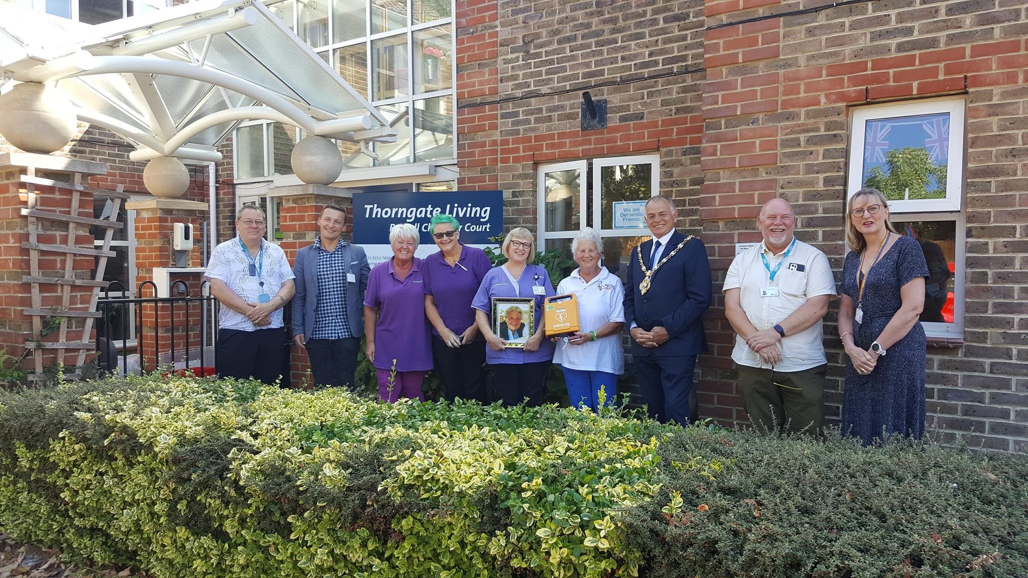 Group photo of staff, community members, and local officials celebrating the donation of a defibrillator at Thorngate Living, a senior care facility.
