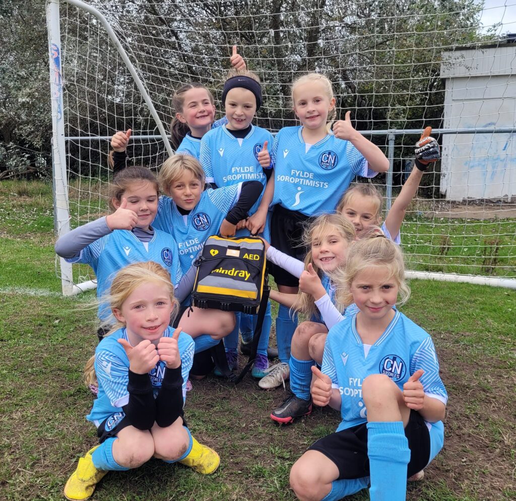 Girls soccer team with an AED bag at a football field, promoting safety and readiness.