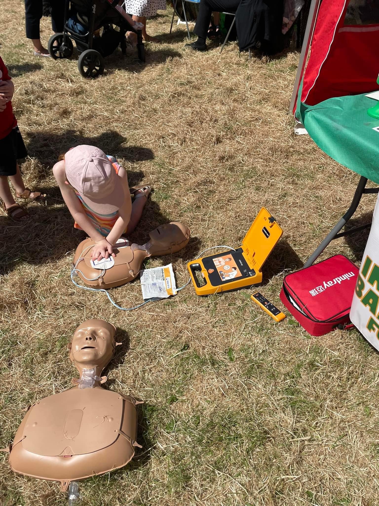Young child practicing CPR on a mannequin with a defibrillator nearby, illustrating the importance of learning life-saving techniques like CPR and defibrillation. Defib World provides defibrillators for public safety and education.