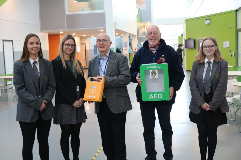 Students and staff holding AED devices in front of the AED station, showcasing the importance of defibrillator availability, featured in the post 'Semi-Automatic vs. Fully Automatic Defibrillators'