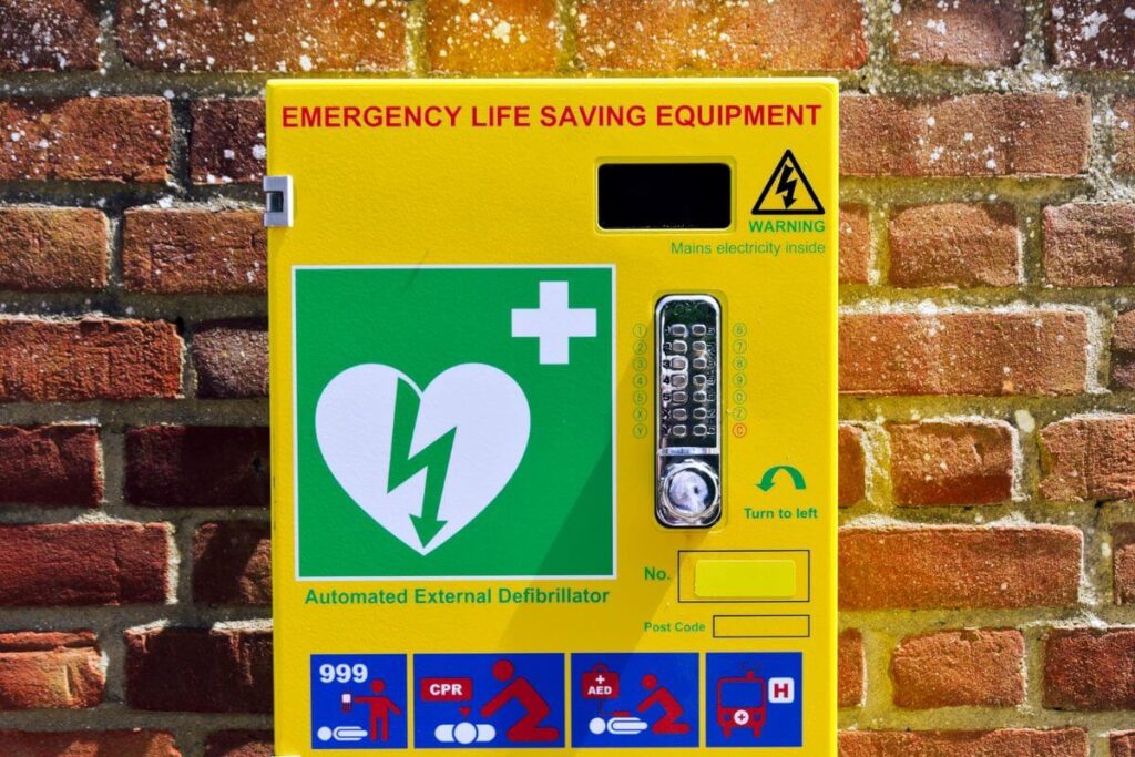 How Much Does A Defibrillator Cost? An automated external defibrillator attached to a red brick wall.