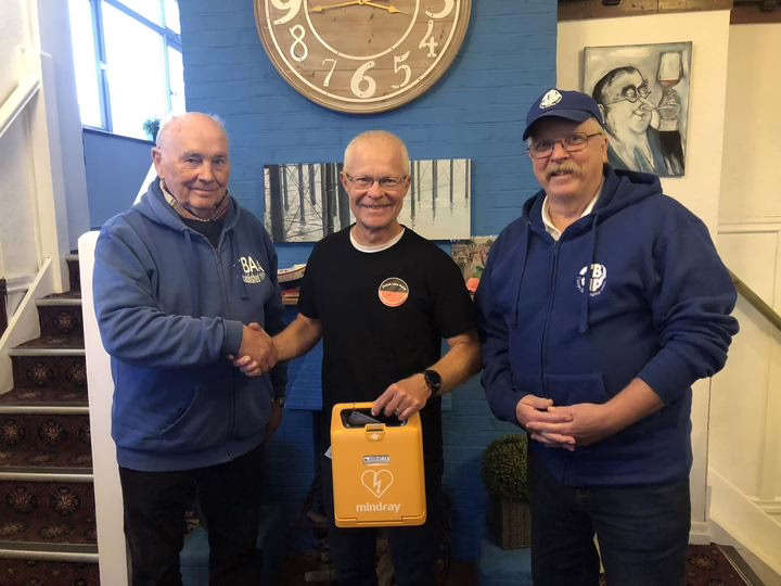 A group of people shaking hands with one holding a Mindray defibrillator in a community setting.