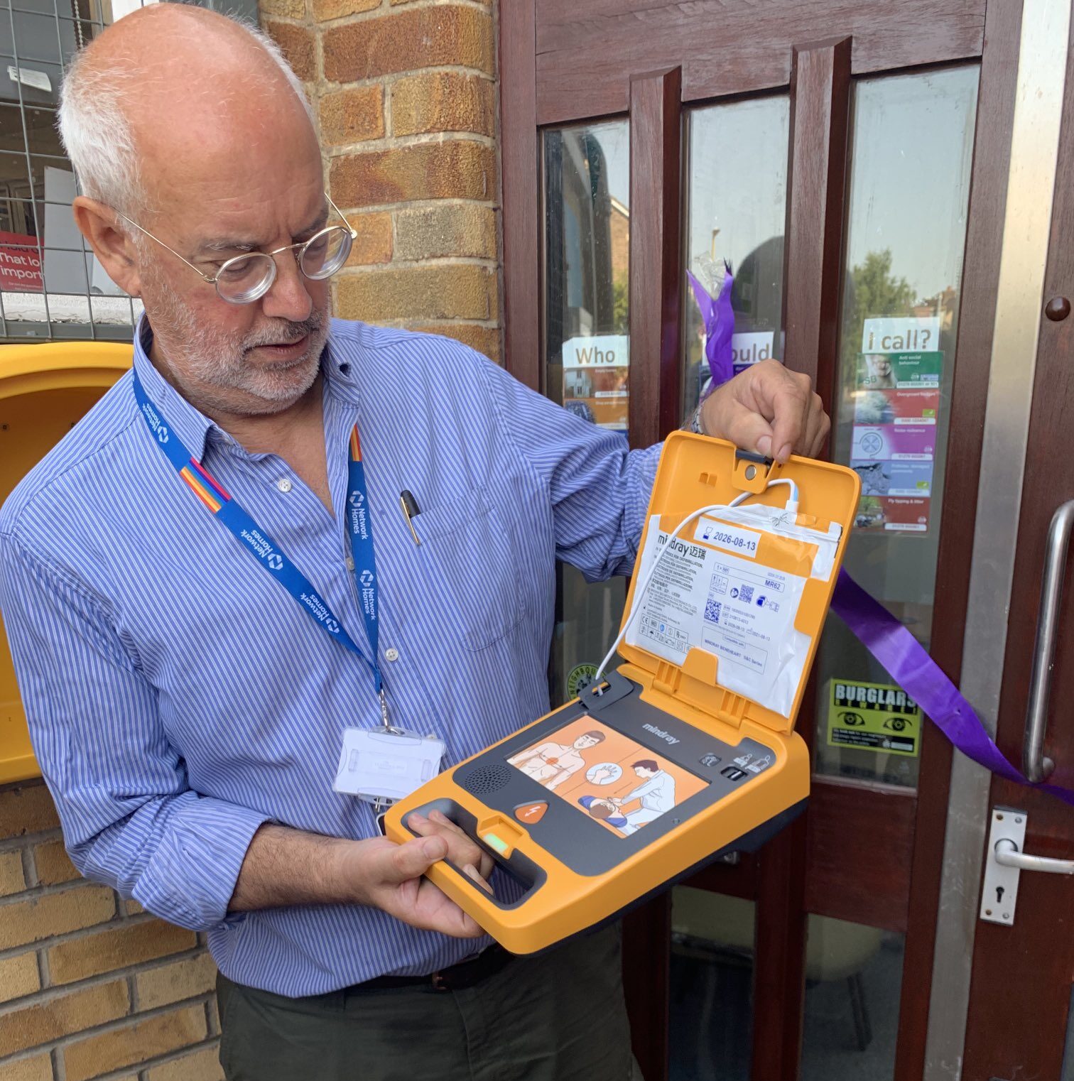 A person showcasing an AED defibrillator, highlighting its easy-to-use features and clear instructions, ideal for various environments such as schools and construction sites.