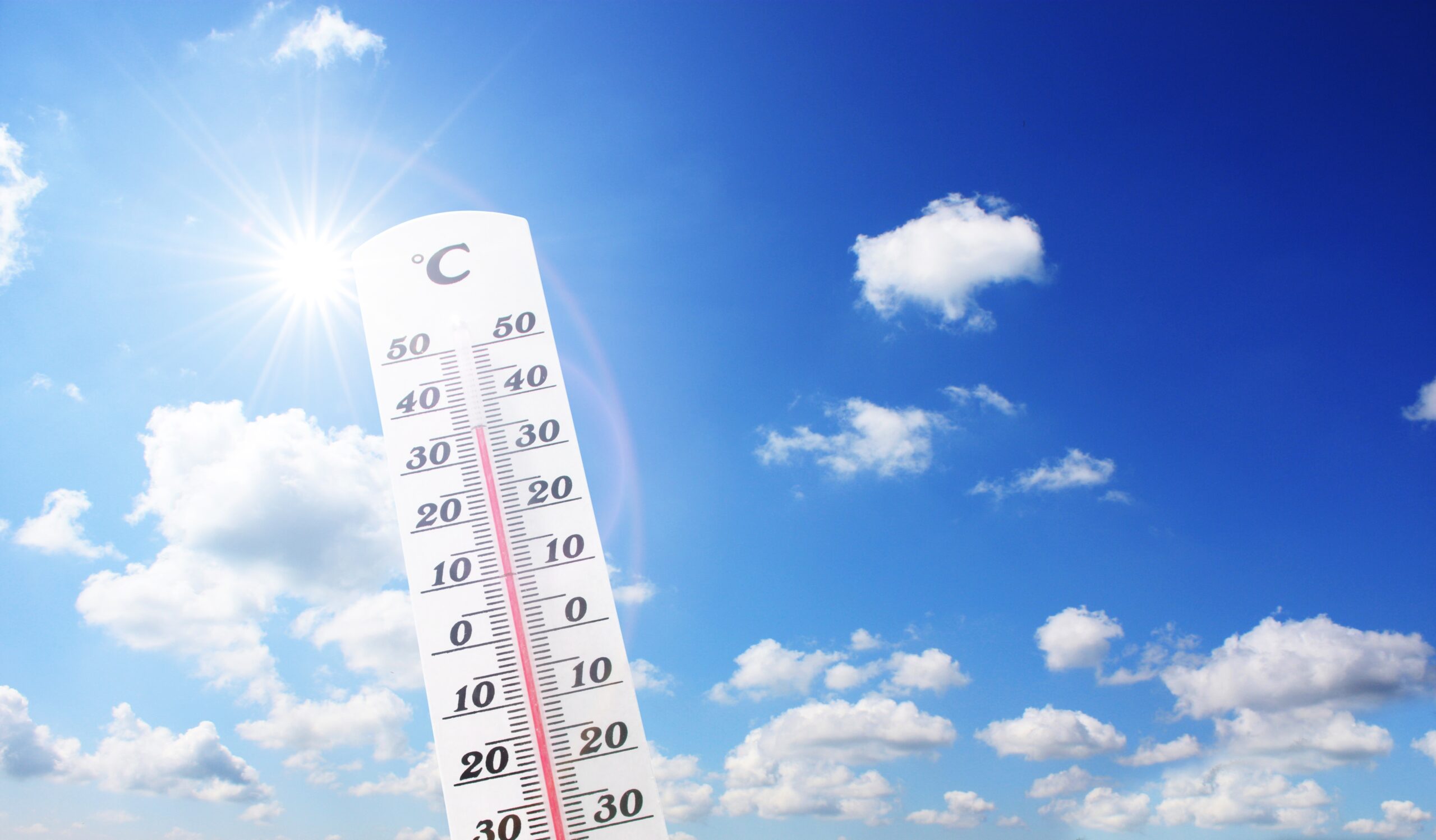 Thermometer showing high temperature under bright sun and blue sky - Highlighting the importance of AEDs in heat-related medical emergencies