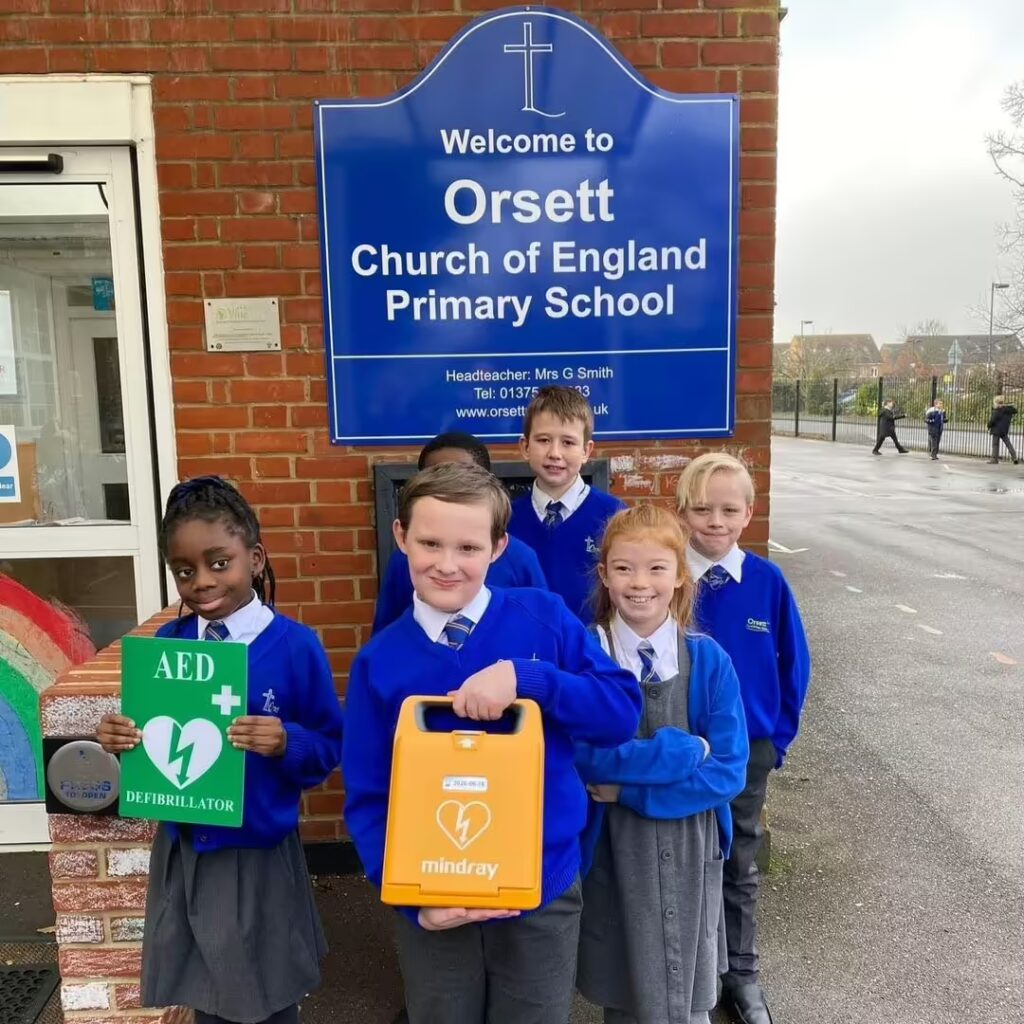 Students from Orsett Church of England Primary School holding an AED device and defibrillator sign, learning about lifesaving techniques as part of their school’s emergency preparedness program.