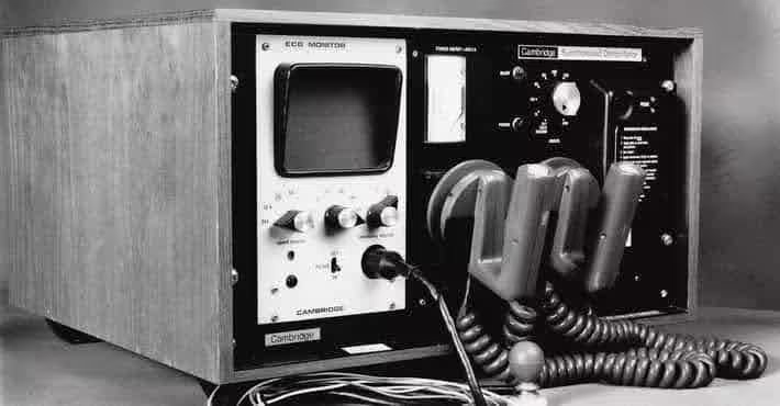 An old, bulky defibrillator machine from the 1960s, with an ECG monitor, dials, and wires. The vintage model showcases the early stages of defibrillation technology, vastly different from modern portable AEDs.