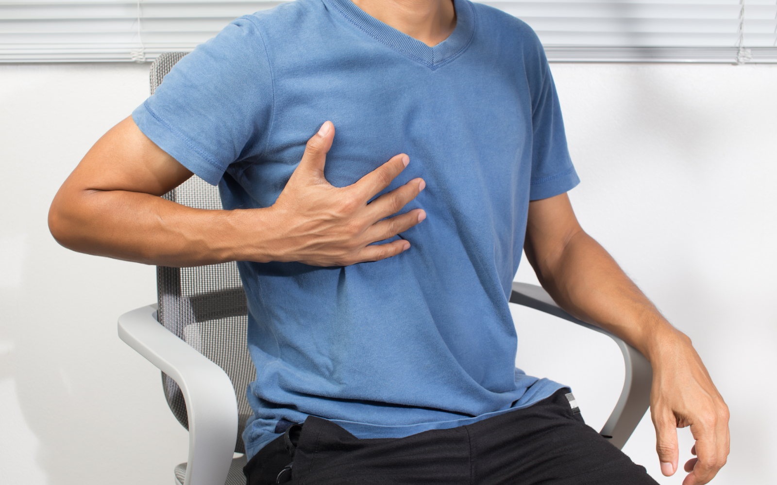 Person holding their chest, indicating signs of chest pain or discomfort commonly associated with a heart attack, a critical symptom of cardiac distress.