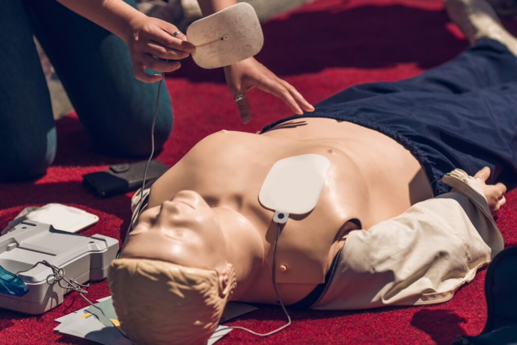 Person placing AED pads on a mannequin during defibrillator training, illustrating the first steps in using an Automated External Defibrillator (AED) during an emergency.